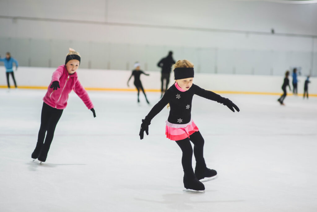 Little girls learning to ice skate. Figure skating school. Young figure skaters practicing at indoor skating rink.